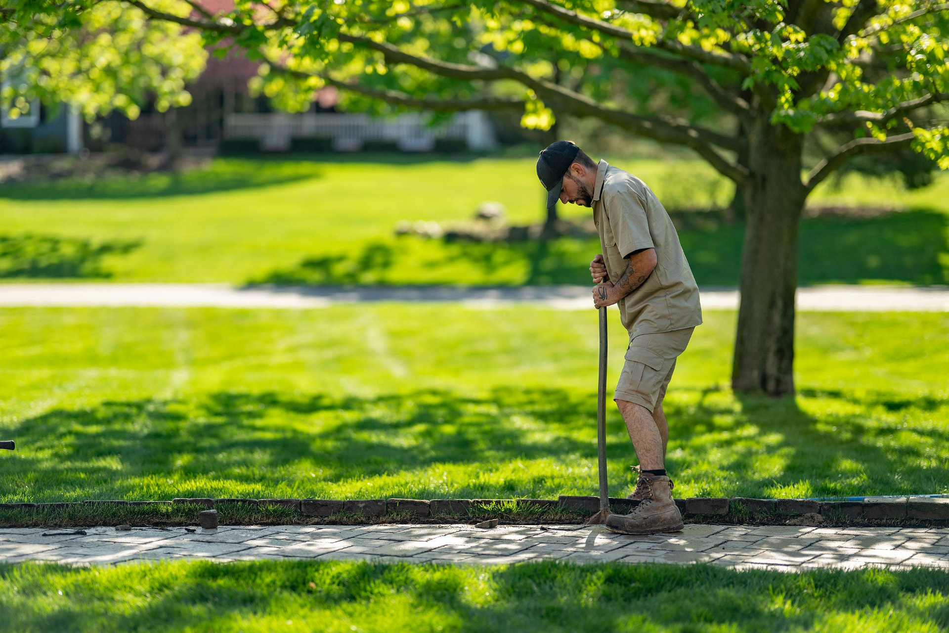 Crew member edging a paver walkway beside a freshly striped lawn