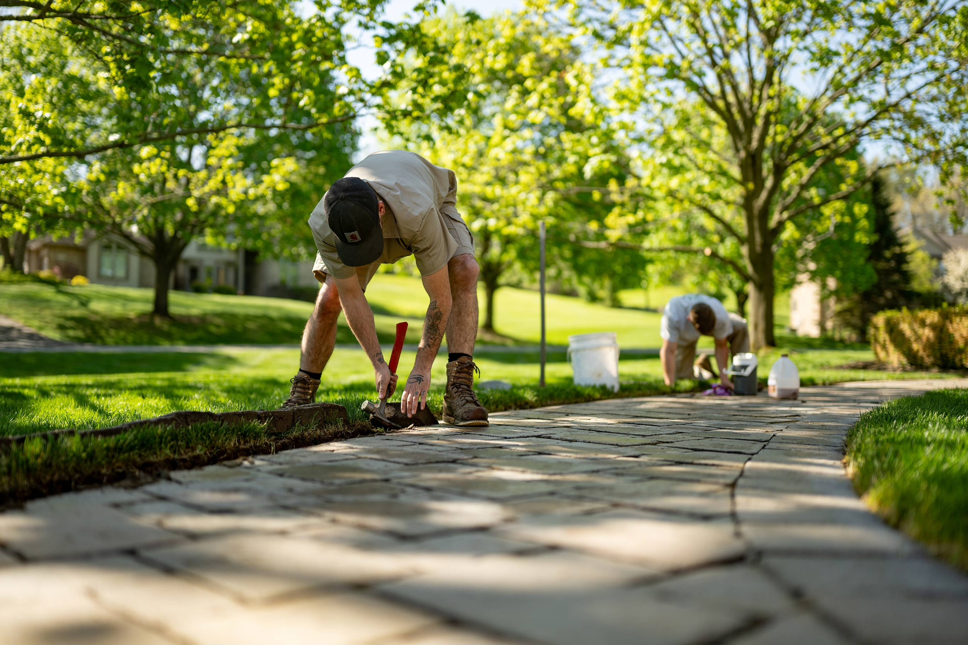 Two Dick's Landscaping crew members repairing a paver walkway edge