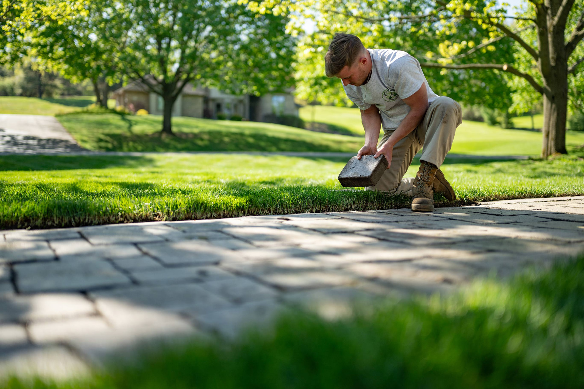 Crew member placing a paver stone along a walkway border