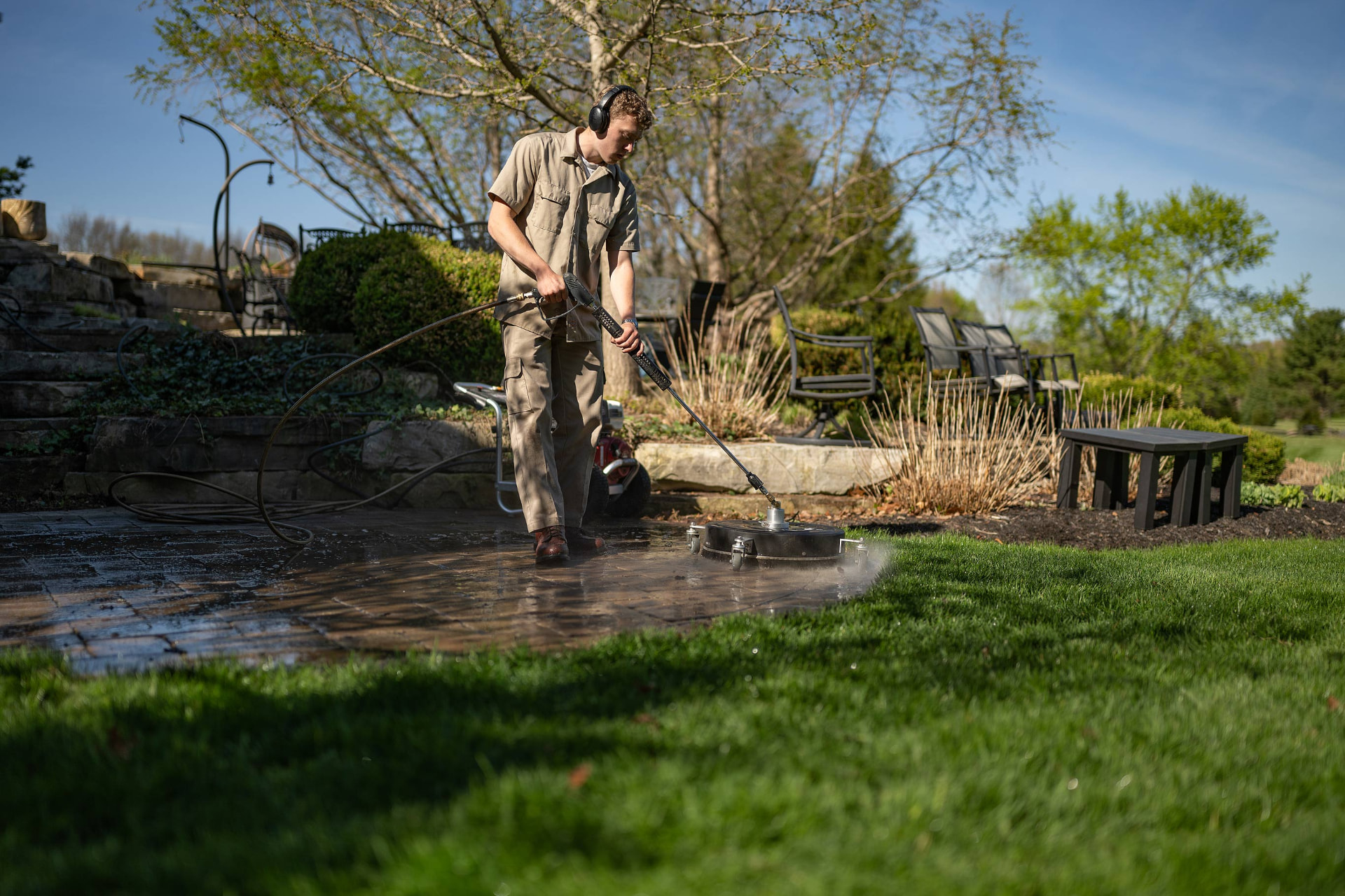 Crew member pressure washing a paver patio with a surface cleaner